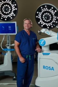 Dr. Malcolm Stubbs in front of the ROSA (robotic surgical assistant) (robotic